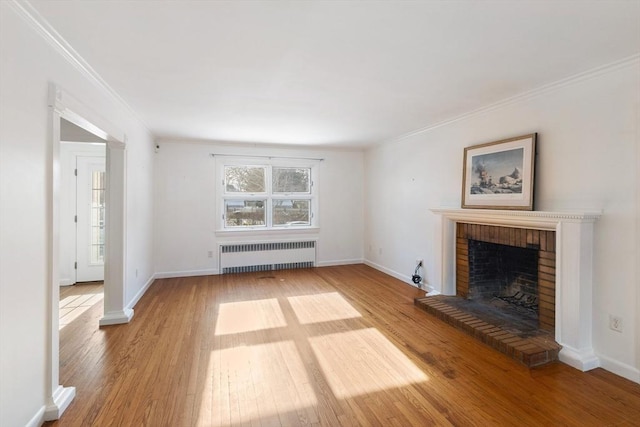 unfurnished living room with a brick fireplace, light hardwood / wood-style floors, radiator, and ornamental molding