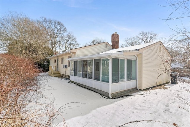 snow covered rear of property featuring a sunroom