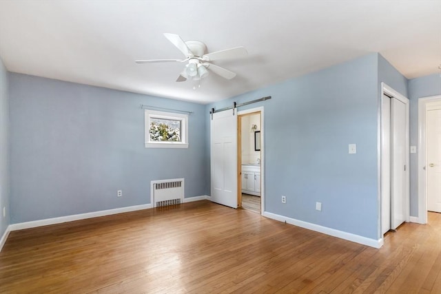 interior space with radiator heating unit, light hardwood / wood-style flooring, ceiling fan, and a barn door