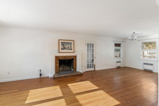 unfurnished living room featuring a notable chandelier, hardwood / wood-style flooring, radiator heating unit, and a brick fireplace