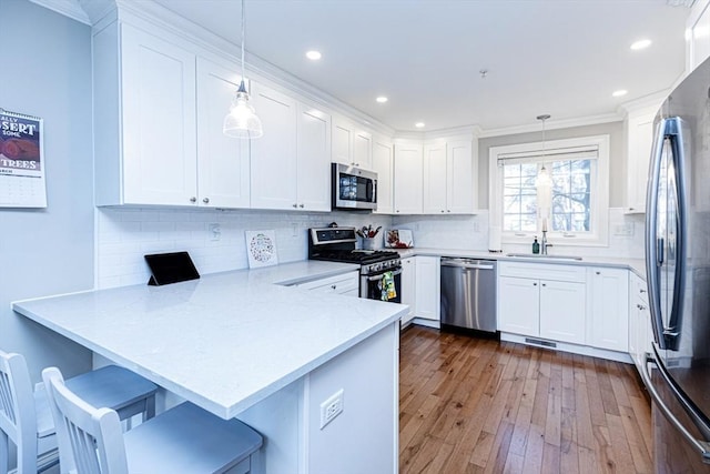 kitchen with a sink, dark wood finished floors, stainless steel appliances, a peninsula, and white cabinets