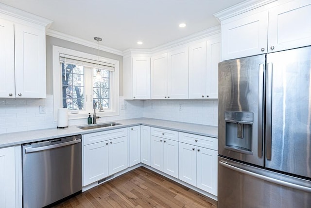 kitchen with ornamental molding, a sink, dark wood finished floors, appliances with stainless steel finishes, and light countertops