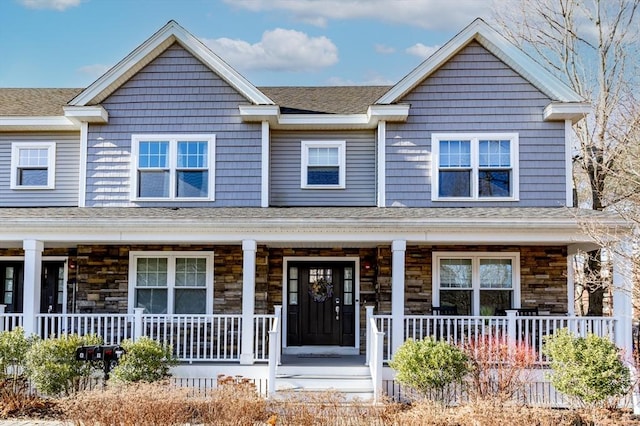 view of front of property with stone siding, covered porch, and a shingled roof