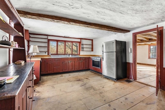 kitchen with appliances with stainless steel finishes, a wealth of natural light, beam ceiling, open shelves, and dark countertops