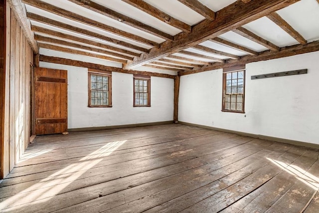 spare room with dark wood-type flooring, baseboards, plenty of natural light, and beamed ceiling