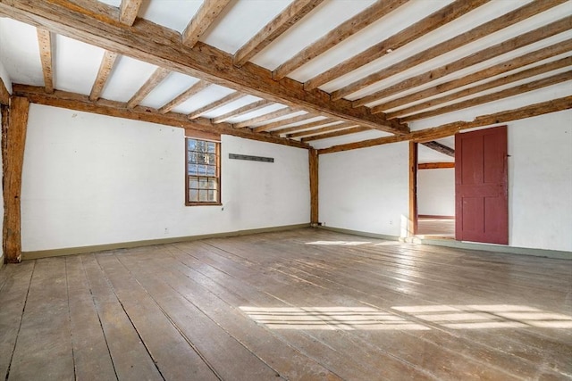 unfurnished room with wood-type flooring, beamed ceiling, and baseboards