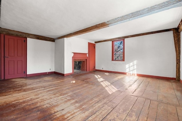 unfurnished living room with beamed ceiling, wood-type flooring, a fireplace, and baseboards