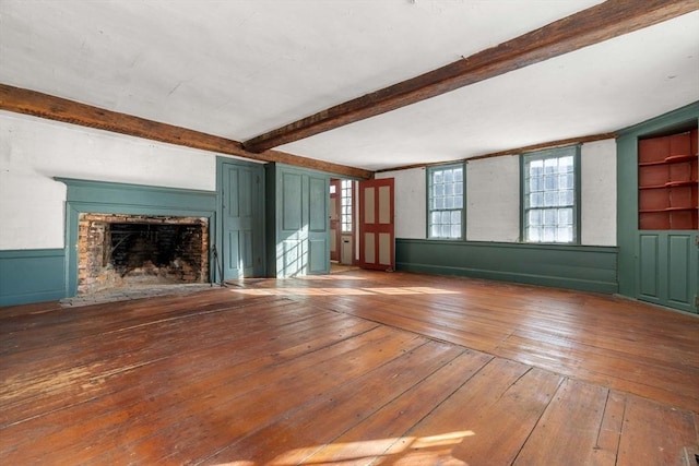 unfurnished living room with a fireplace with flush hearth, a wainscoted wall, beamed ceiling, and hardwood / wood-style floors