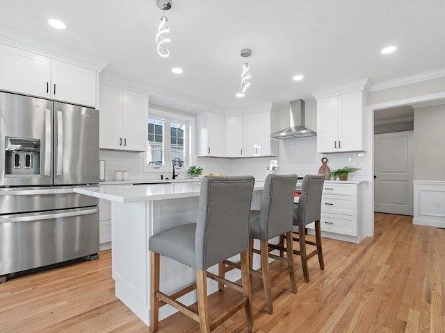 kitchen with decorative light fixtures, wall chimney exhaust hood, stainless steel fridge with ice dispenser, and white cabinetry