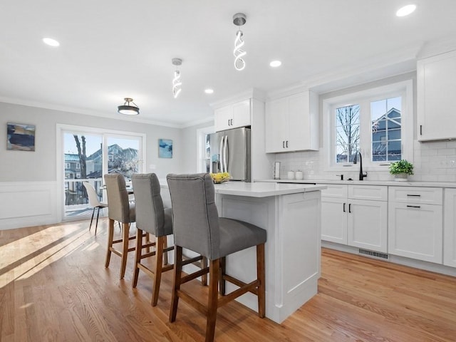 kitchen with pendant lighting, white cabinets, a kitchen island, stainless steel fridge with ice dispenser, and ornamental molding