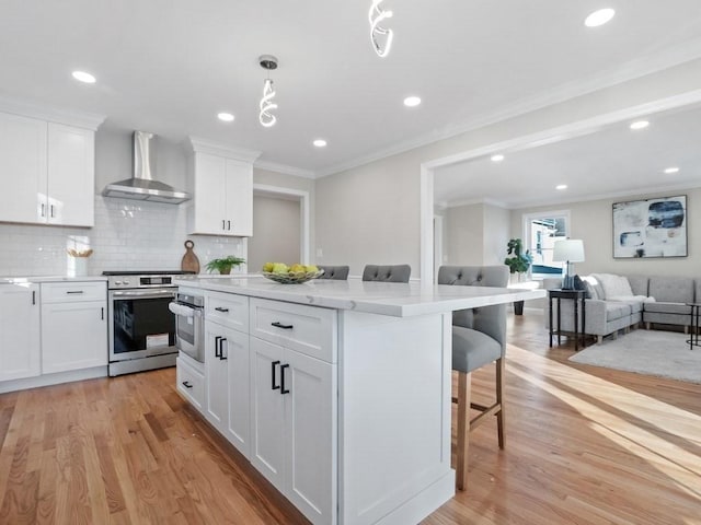 kitchen with a kitchen breakfast bar, appliances with stainless steel finishes, wall chimney exhaust hood, and white cabinetry