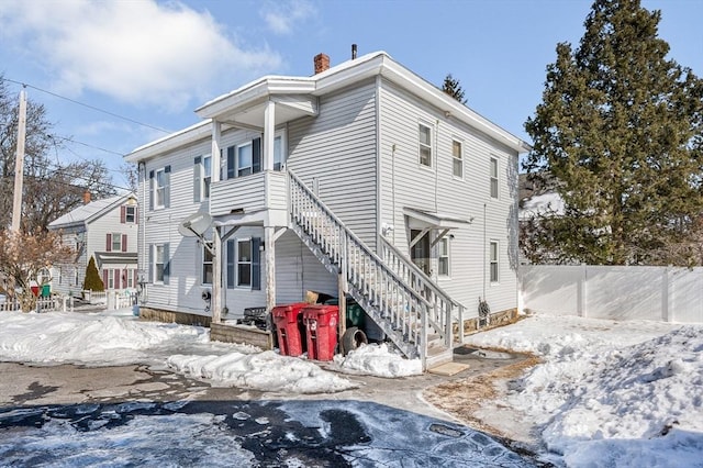 snow covered property featuring fence and a chimney