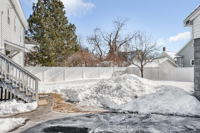 yard covered in snow with a fenced backyard and stairs