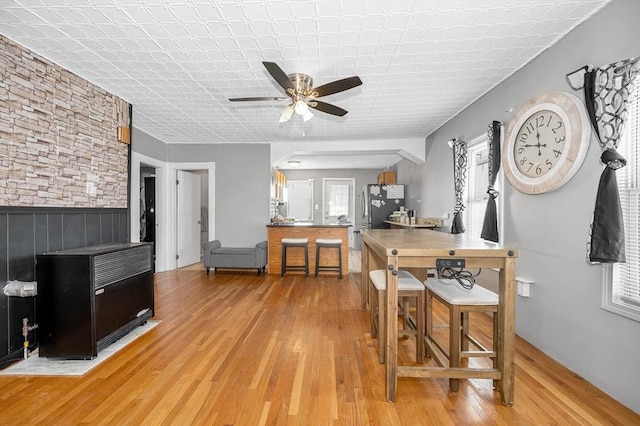 dining area with a ceiling fan, a wainscoted wall, and light wood finished floors