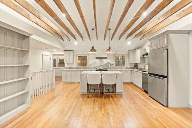 kitchen with appliances with stainless steel finishes, decorative light fixtures, beam ceiling, a kitchen bar, and a center island