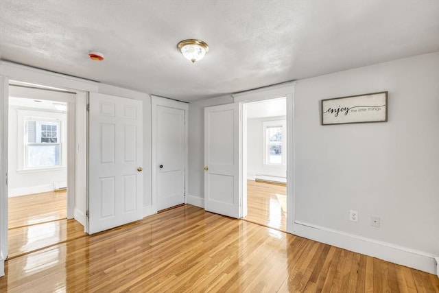 unfurnished bedroom with multiple windows, a baseboard radiator, a textured ceiling, and light wood-type flooring