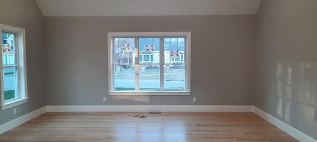 unfurnished room featuring vaulted ceiling, light wood-type flooring, and a healthy amount of sunlight