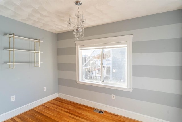 empty room with hardwood / wood-style flooring and a chandelier