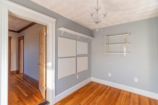 empty room with hardwood / wood-style flooring, crown molding, and a notable chandelier