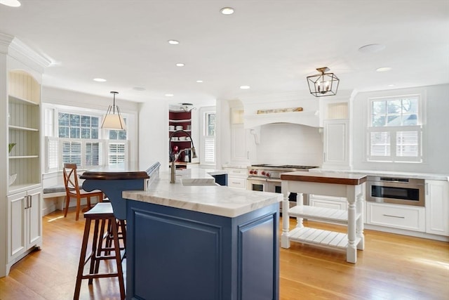 kitchen with an island with sink, pendant lighting, white cabinets, and light hardwood / wood-style flooring