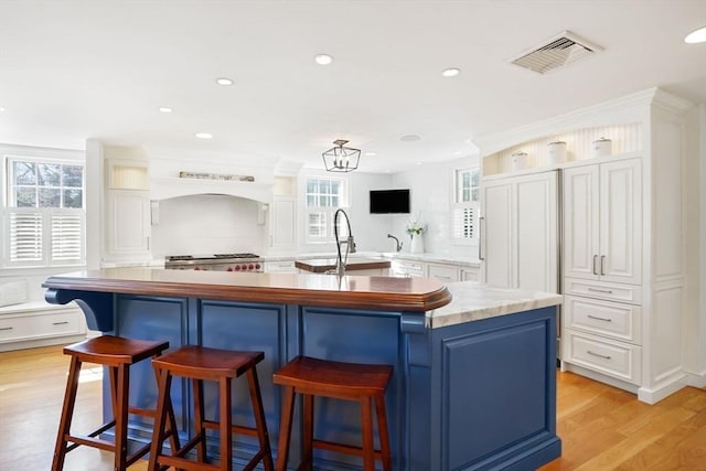 kitchen with sink, a breakfast bar area, a kitchen island with sink, white cabinets, and light wood-type flooring