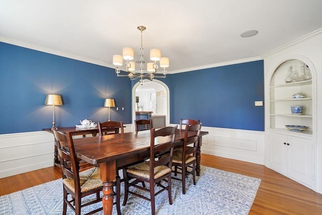 dining area with a notable chandelier, crown molding, built in features, and light hardwood / wood-style floors