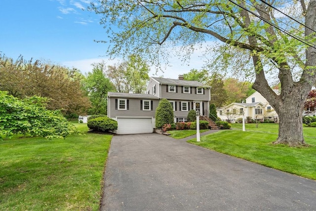 colonial inspired home with a chimney, a garage, driveway, and a front yard