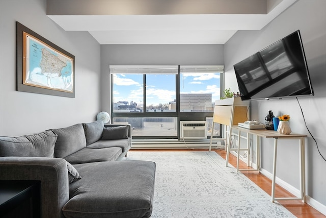 living room featuring a wall mounted air conditioner, hardwood / wood-style flooring, and a baseboard heating unit