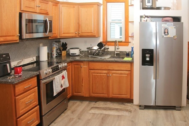 kitchen with dark stone countertops, stainless steel appliances, light wood-style flooring, and a sink