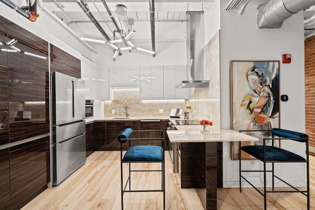 kitchen featuring a breakfast bar, backsplash, ventilation hood, appliances with stainless steel finishes, and white cabinetry