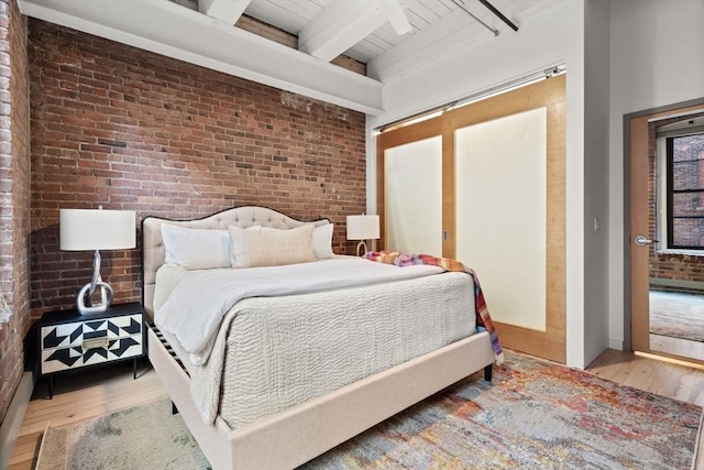 bedroom featuring wooden ceiling, ceiling fan, beamed ceiling, light hardwood / wood-style floors, and brick wall