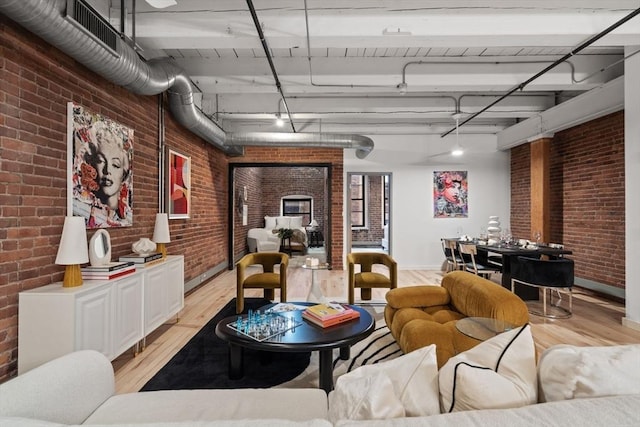 living room featuring beamed ceiling, light wood-type flooring, and brick wall