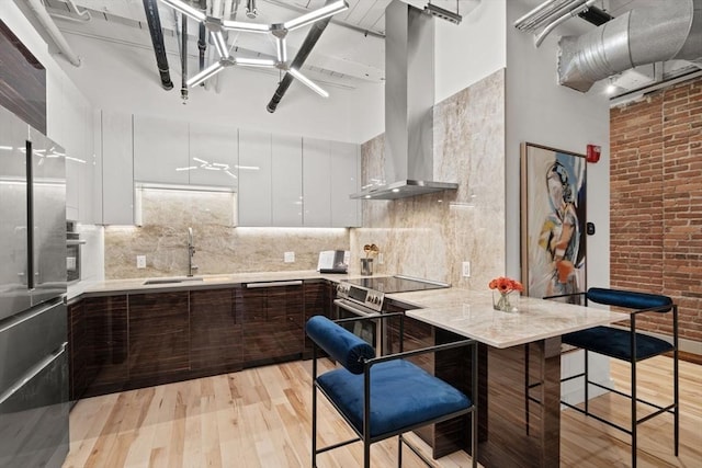 kitchen with dark brown cabinetry, white cabinetry, sink, a high ceiling, and range hood