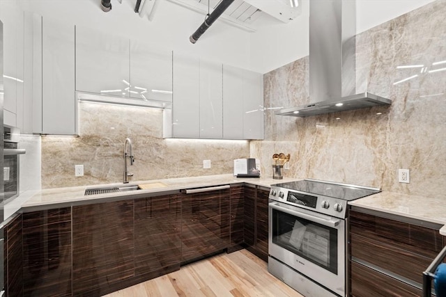 kitchen featuring appliances with stainless steel finishes, backsplash, wall chimney exhaust hood, light hardwood / wood-style floors, and white cabinetry