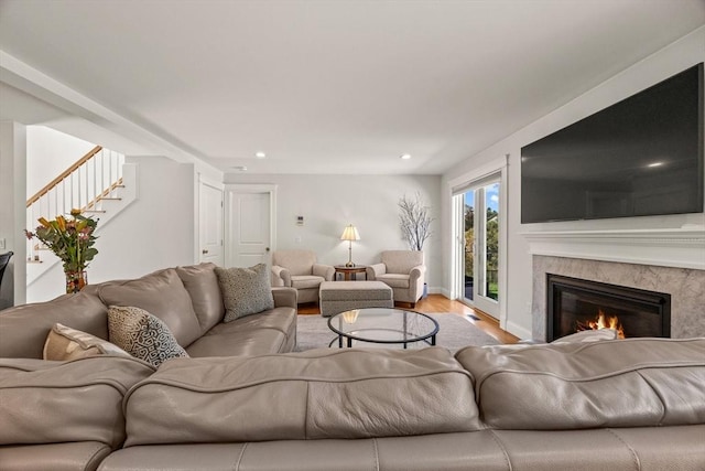 living room featuring a premium fireplace, light wood-style flooring, stairway, recessed lighting, and baseboards