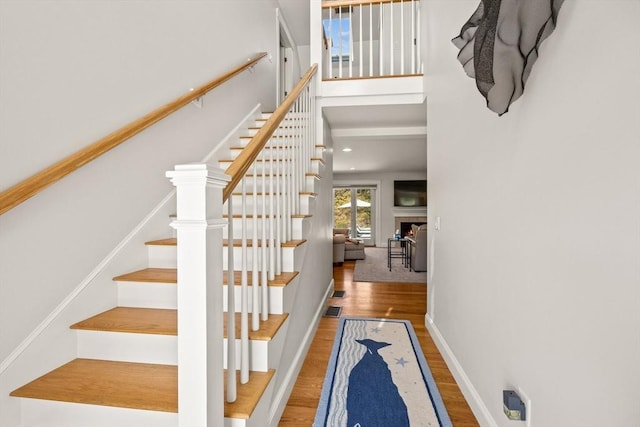 stairway featuring wood finished floors, a towering ceiling, baseboards, and a fireplace