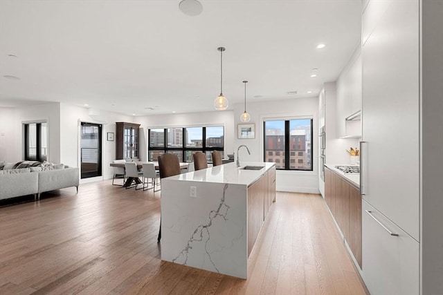 kitchen featuring white cabinetry, an island with sink, sink, hanging light fixtures, and light hardwood / wood-style flooring