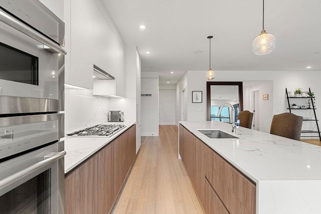 kitchen featuring decorative light fixtures, white cabinetry, sink, light hardwood / wood-style floors, and stainless steel appliances