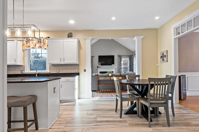 dining space featuring lofted ceiling, recessed lighting, a fireplace, light wood-type flooring, and decorative columns