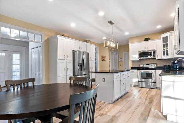 kitchen with decorative backsplash, light wood-style flooring, a kitchen island, appliances with stainless steel finishes, and white cabinetry