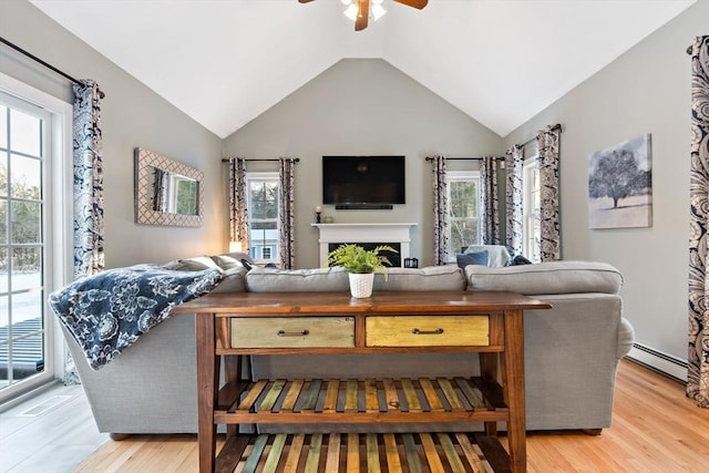 living area featuring lofted ceiling, a baseboard radiator, ceiling fan, light wood-type flooring, and a fireplace