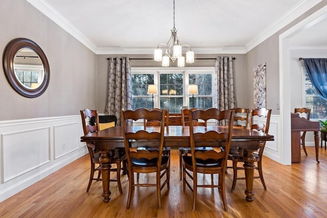 dining space with light wood finished floors, a chandelier, crown molding, and a wainscoted wall