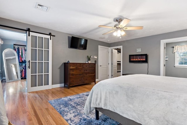 bedroom with light wood finished floors, a spacious closet, a barn door, and visible vents