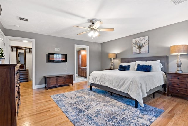 bedroom with light wood finished floors, baseboards, visible vents, connected bathroom, and a ceiling fan