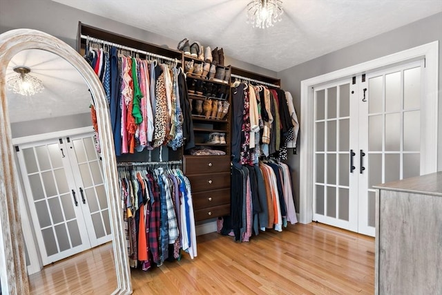 walk in closet featuring french doors, wood finished floors, and a notable chandelier