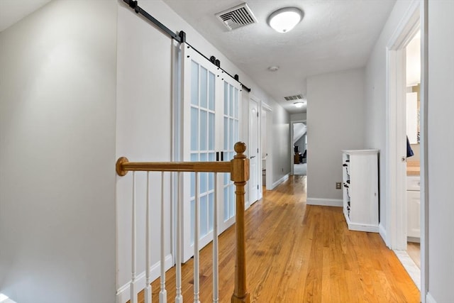 corridor with light wood-style floors, a barn door, visible vents, and baseboards