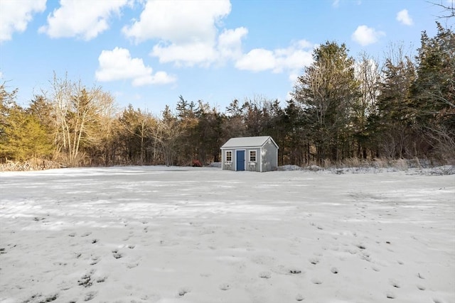 snowy yard featuring a storage unit, an outdoor structure, and a view of trees