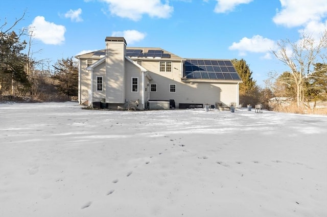 back of property with roof mounted solar panels and a chimney