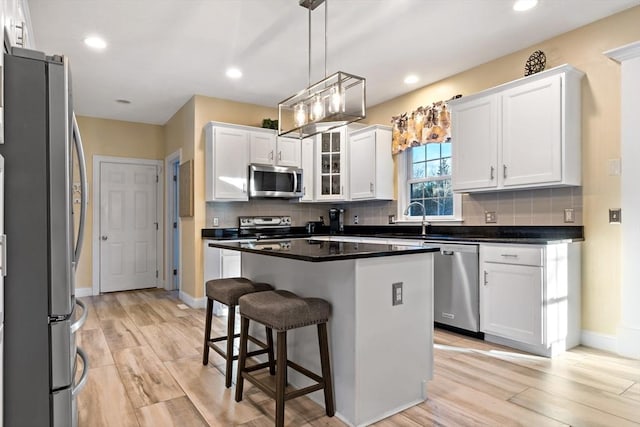 kitchen with white cabinets, decorative backsplash, appliances with stainless steel finishes, a kitchen bar, and a sink