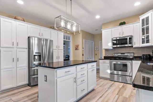 kitchen with white cabinets, light wood-style floors, stainless steel appliances, and decorative backsplash